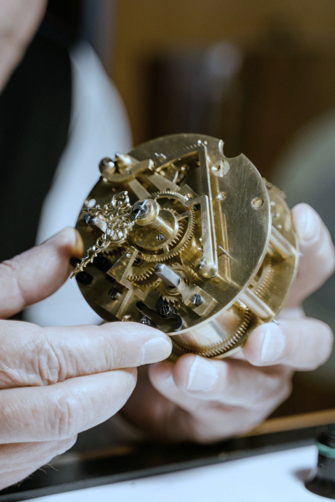 A golden clockwork movement held and examined in careful hands