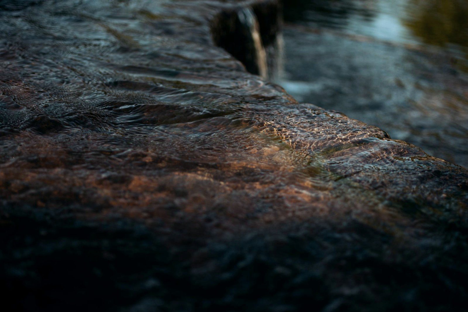 Water moving over dark stone, gold light held in the ripples