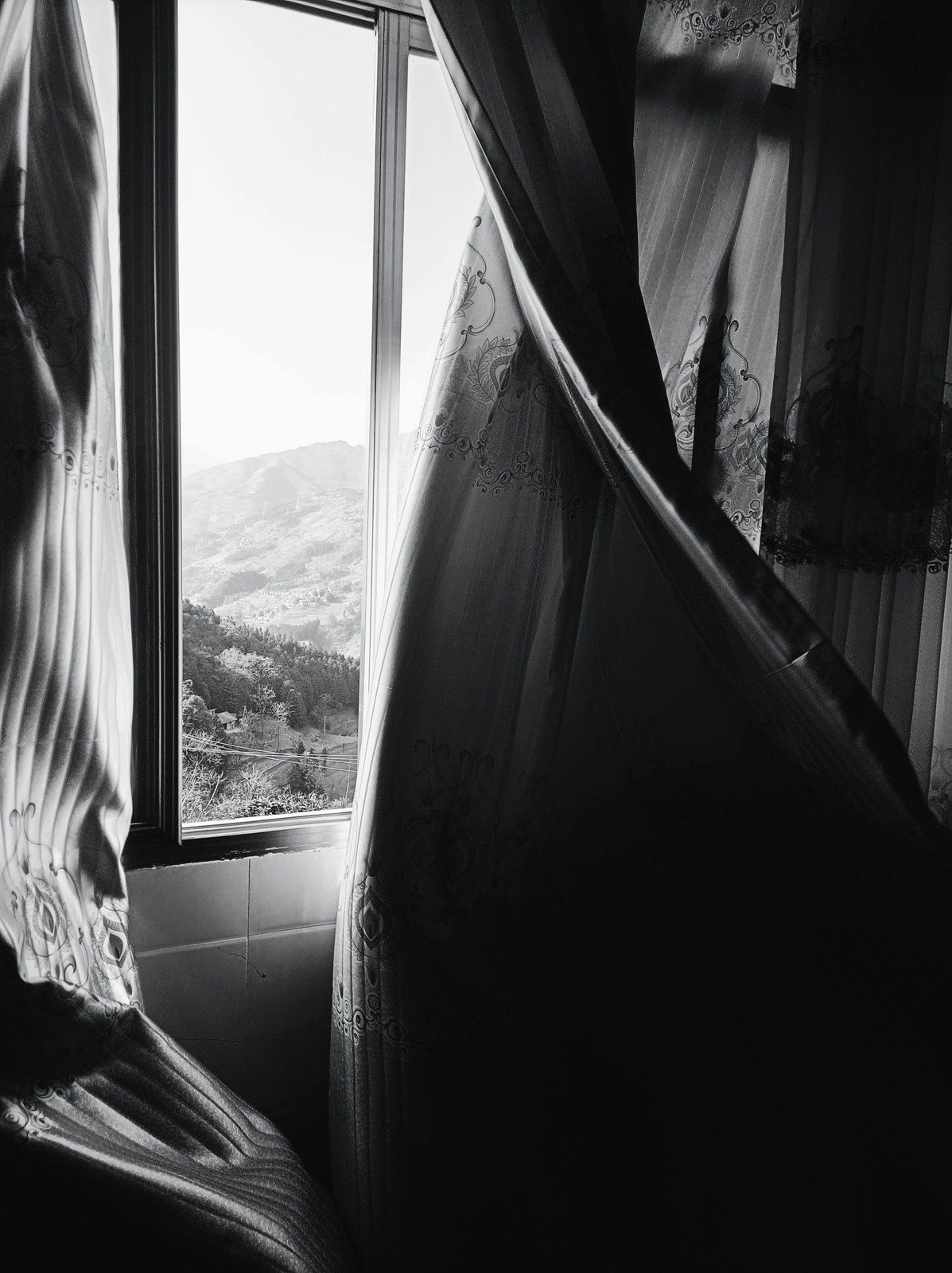 Light breaking into a dark room through a parted curtain, mountains beyond