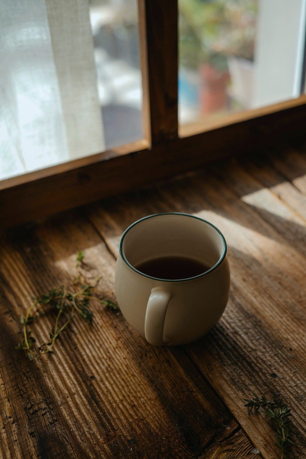 A cup of tea in the sun on a wooden sill, fresh herbs beside it